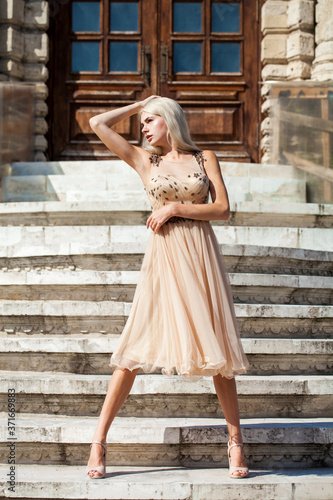 young beautiful girl in beige dress posing on the stone steps