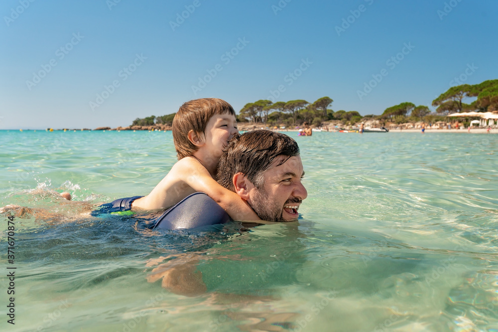 Father and little son having fun swimming together in sea water at summer holidays on Corsica. Family bonding, togetherness. Seaside vacation. Palombaggia beach