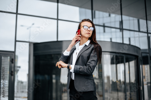 A business woman checks the time and talking on the phone in the city during a working day waiting for a meeting. Discipline and timing. An employee goes towards a corporate meeting.