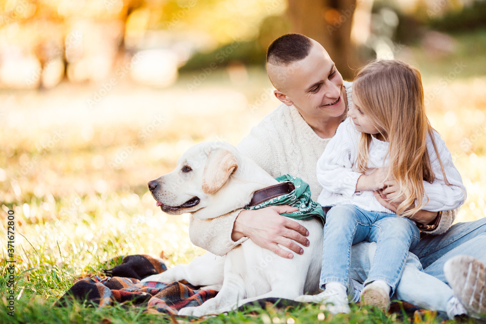 Happy father and daughter with dog labrador is having fun are sitting on green grass in park. Happy father and daughter with dog labrador is having fun are sitting on green grass in park.