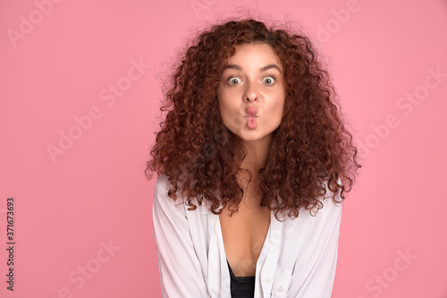 Cute young girl with foxy curly hair making funny face over pink background. Copy space.