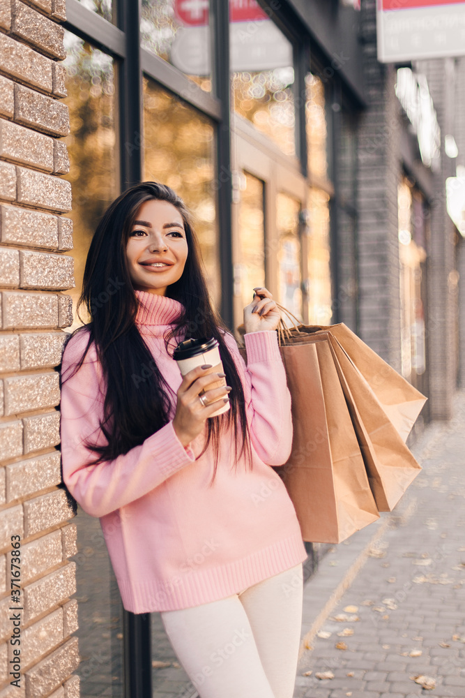 Beautiful smiling young woman with shopping  bags and coffee on the street.