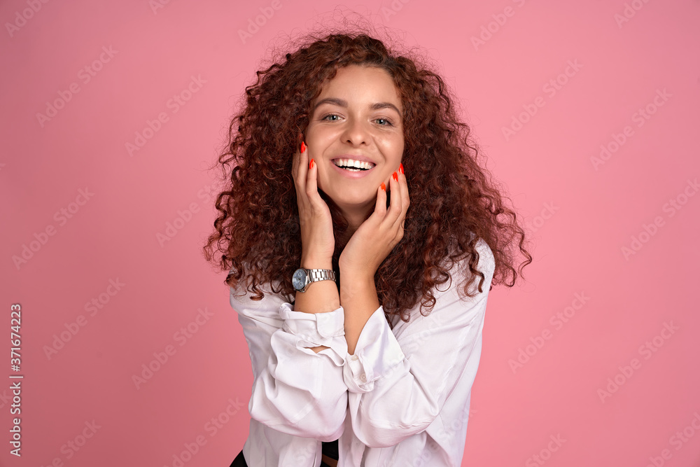 Pretty cheerful redhead girl with flying curly hair smiling laughing looking at camera over pink background. Pretty cheerful redhead girl with flying curly hair smiling laughing looking at camera over pink background.