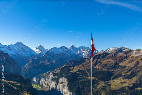 Panorama view of Swiss Alps on Bernese Oberland, Breithorn and Schilthorn, view of Lauterbrunnen valley and Swiss national flag in foreground, autumn day, from Mannlichen, Canton Bern, Switzerland