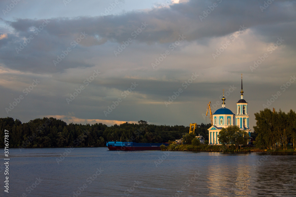 Dramatic landscape-Orthodox Church and green trees on the Bank of the Volga river with reflection on the background of a stormy sky with beautiful clouds