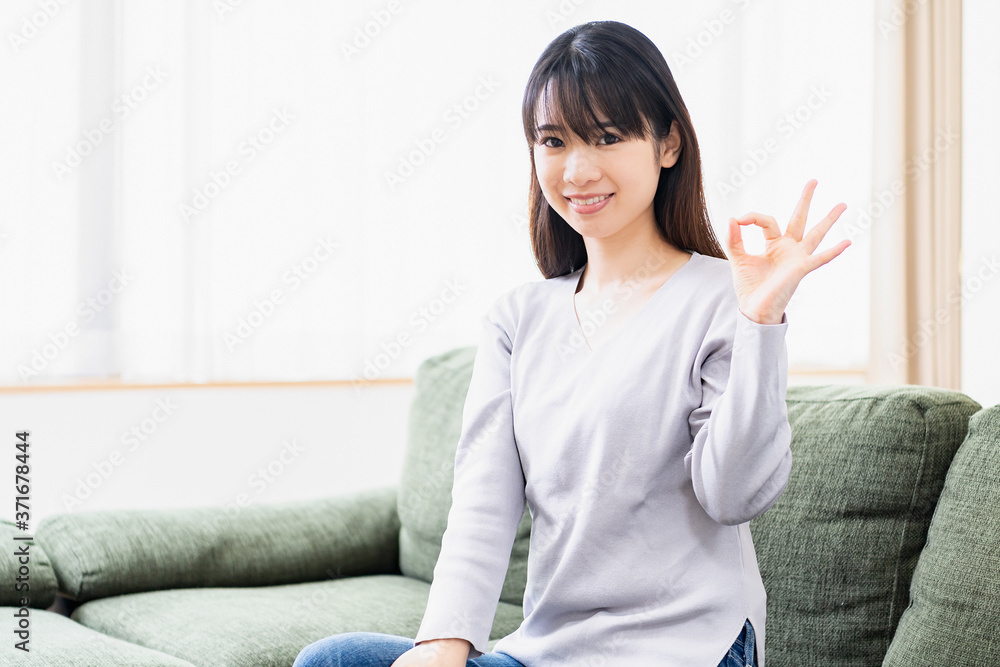 リビングのソファでOKのジェスチャーをする若い女性
