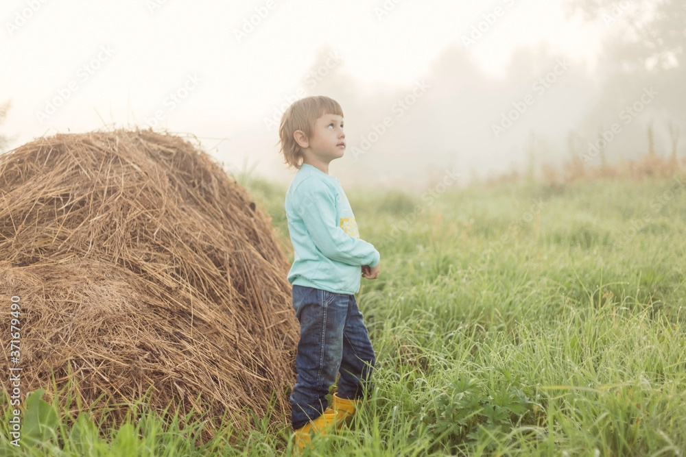 A girl stands next to a stack of dry grass against a foggy landscape A girl stands next to a stack of dry grass against a foggy landscape
