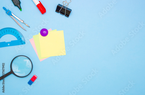 The concept of school and students. Empty square colored paper for writing in the middle. School and office stationery on the edges on a blue background. Top view, free space for text.