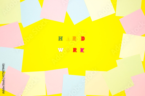 The concept of motivation, work. The words HARD WORK in the center on a yellow background, colored letters. Frame from empty note papers. Top view. photo