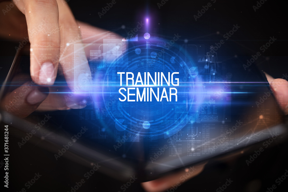 Young man holding a foldable smartphone with TRAINING SEMINAR inscription, educational concept Young man holding a foldable smartphone with TRAINING SEMINAR inscription, educational concept