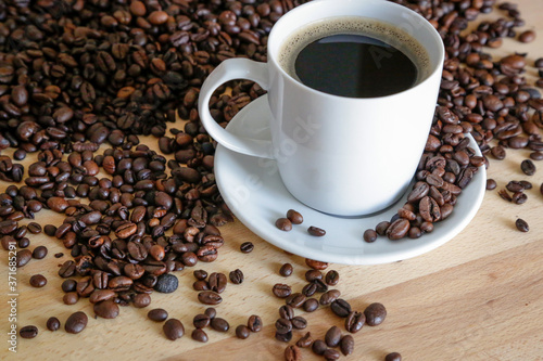  A cup of black coffee with coffee grains, natural light on wooden table