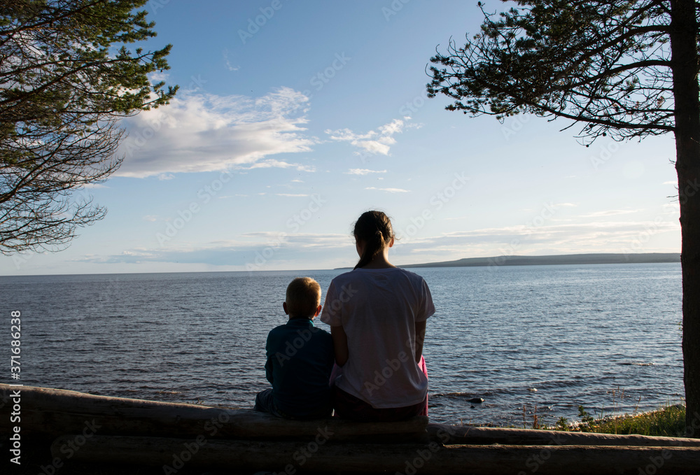 Brother and sister sit by the sea in a pine forest and looking the sunset