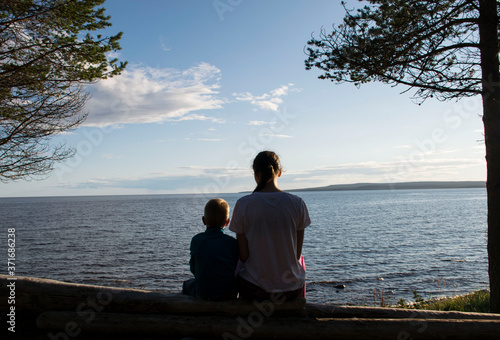 Brother and sister sit by the sea in a pine forest and looking the sunset