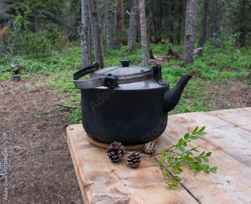 A camping kettle stands on a wooden table in the forest or in the countryside