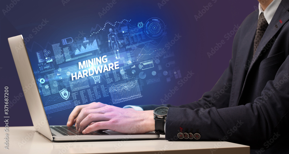 Businessman working on laptop with MINING HARDWARE inscription, cyber technology concept Businessman working on laptop with MINING HARDWARE inscription, cyber technology concept
