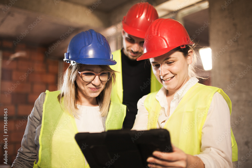 team of engineers in vests and hard hats with in a tablet, on a construction site team of engineers in vests and hard hats with in a tablet, on a construction site