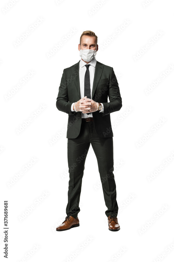 Blonde attractive businessman wearing a dark suit with a grey tie and a face mask covering his mouth and nose. Standing against a white background. Blonde attractive businessman wearing a dark suit with a grey tie and a face mask covering his mouth and nose. Standing against a white background.