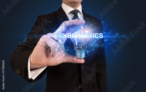 Businessman holding light bulb with CYBERNETICS inscription, innovative technology concept