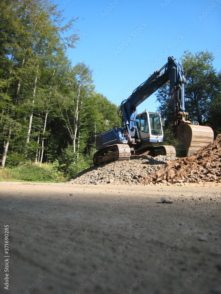Obraz premium Blauer Bagger auf dem Waldparkplatz