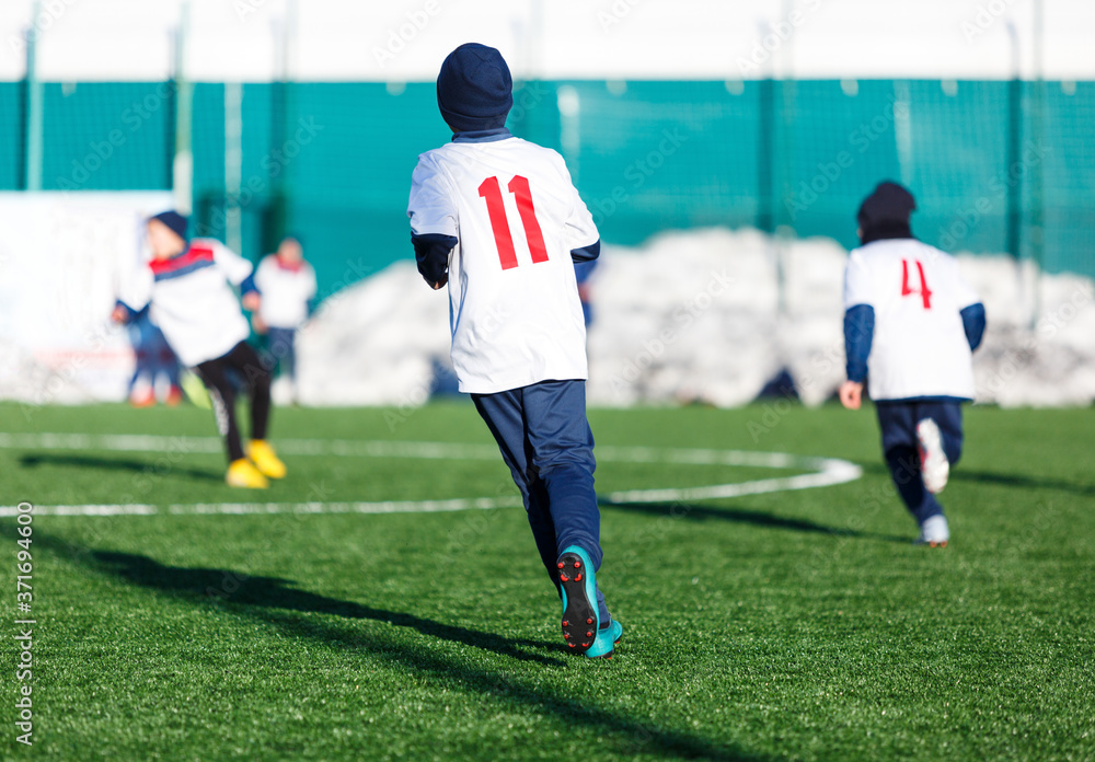 Boys in white red sportswear running on soccer field with snow on background. Young footballers dribble and kick football ball in game. Training, active lifestyle, sport, children winter activity 