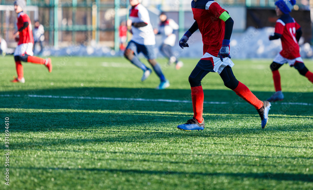 Boys in white red sportswear running on soccer field with snow on background. Young footballers dribble and kick football ball in game. Training, active lifestyle, sport, children winter activity Boys in white red sportswear running on soccer field with snow on background. Young footballers dribble and kick football ball in game. Training, active lifestyle, sport, children winter activity