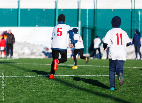 Boys in white red sportswear running on soccer field with snow on background. Young footballers dribble and kick football ball in game. Training, active lifestyle, sport, children winter activity 