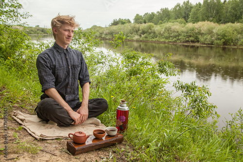 Young man with blonde hair drinking chinese tea in summer park