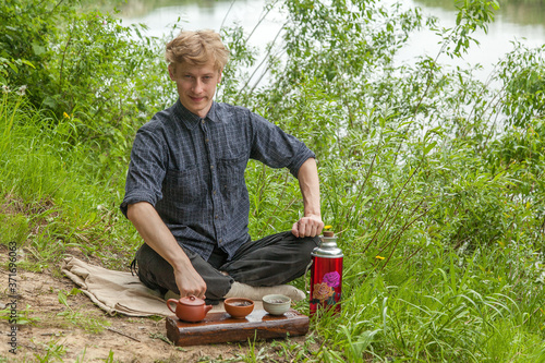 Young man with blonde hair drinking chinese tea in summer park