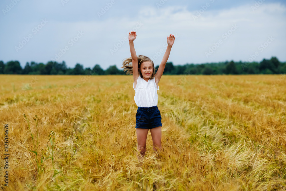 A happy and smiling girl jumps with her hands in the air in a wheat field A happy and smiling girl jumps with her hands in the air in a wheat field