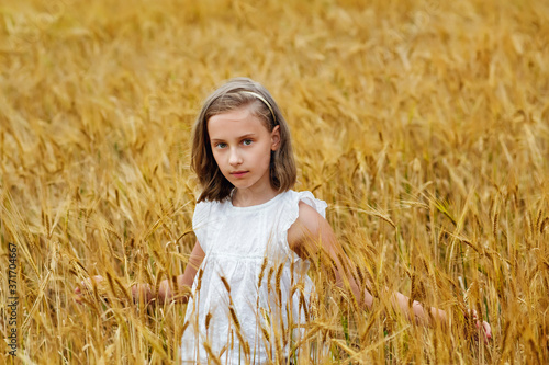 Large portrait of a girl sitting in a wheat field with wheat ears in her hands.
