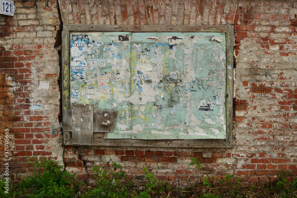 Old dirty wooden board with scraps of advertisements on a vintage red brick wall.