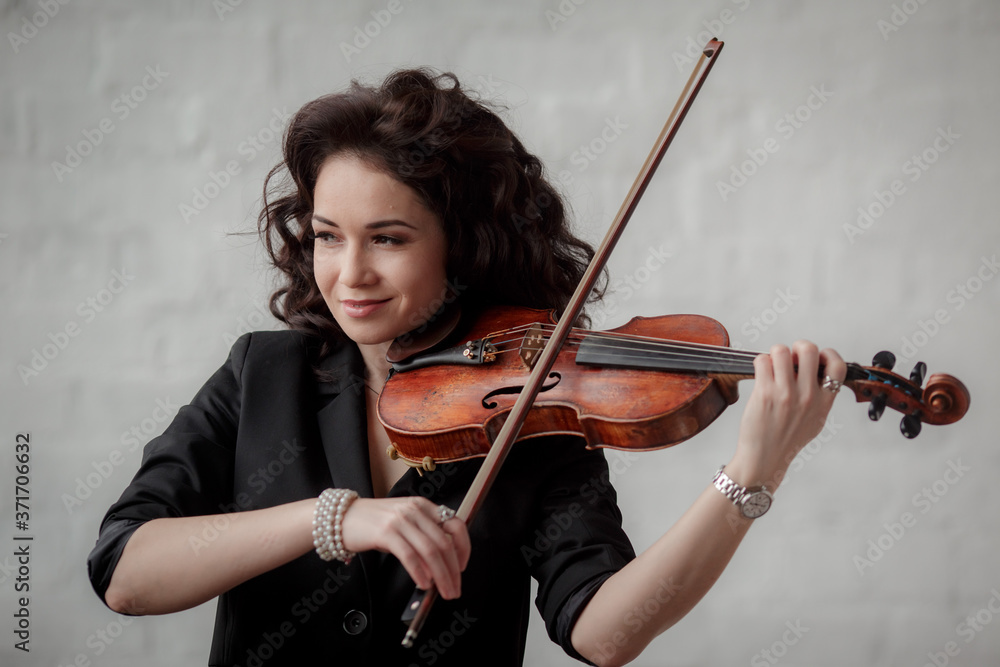 Young attractive brunette girl of Asian appearance on a white brick background with a violin in her hands.