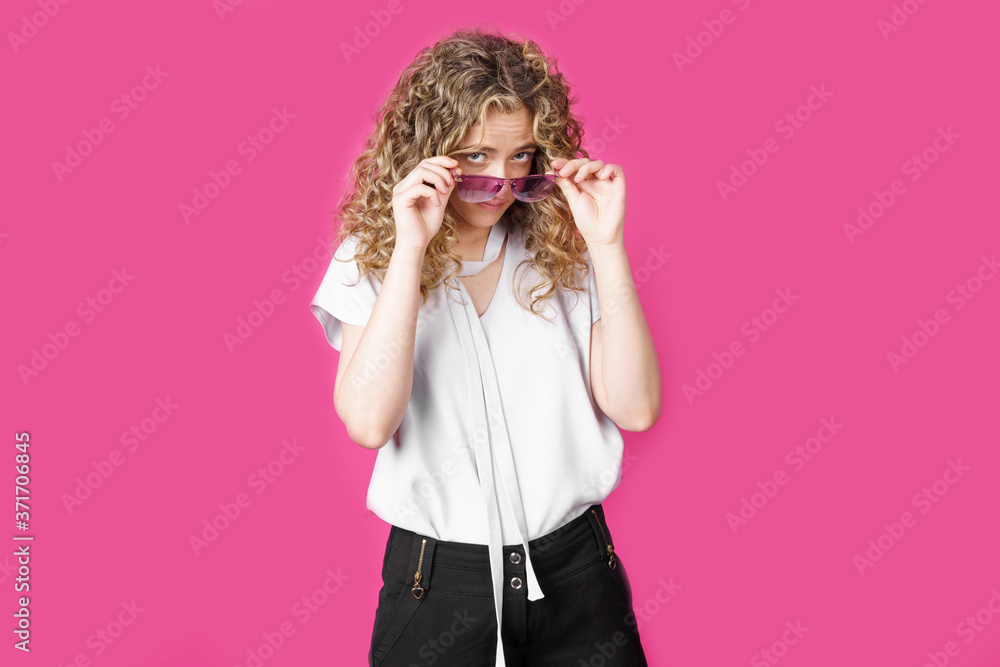 A young woman holds glasses with her hands and looks from under them. A young woman holds glasses with her hands and looks from under them.