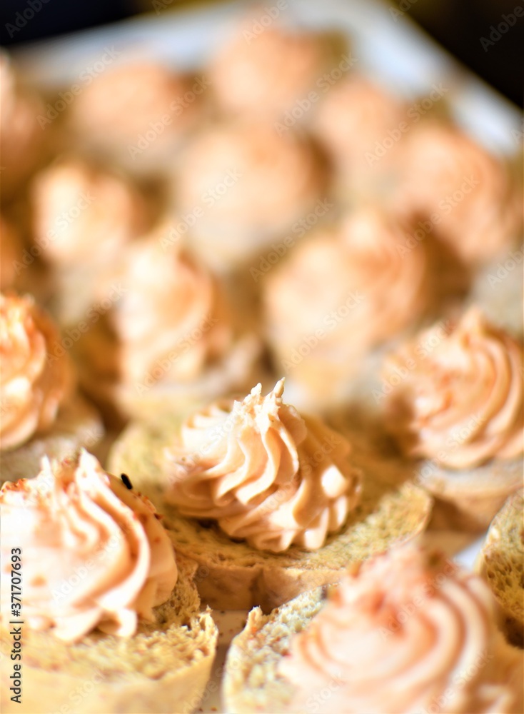 Cookies decorated with twirling creamy frosting on top served on a white plate at a cocktail party Cookies decorated with twirling creamy frosting on top served on a white plate at a cocktail party
