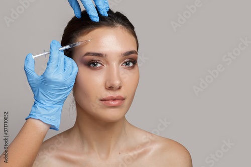 Portrait of a woman with clean skin on a gray background. Needle insertion for mesotherapy. Smoothing wrinkles. copycpase photo