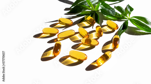 Herbal dietary supplements and vitamins D, A or E  decorated with green leaves on white background. Gelatin softgels. Concept of healthcare and alternative medicine: homeopathy and naturopathy photo