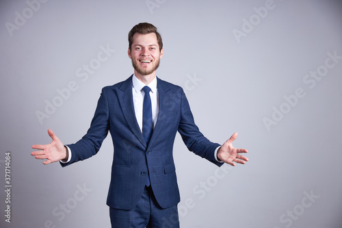 A businessman in a blue office business suit has turned his arms to the sides, looks into the camera and smiles.