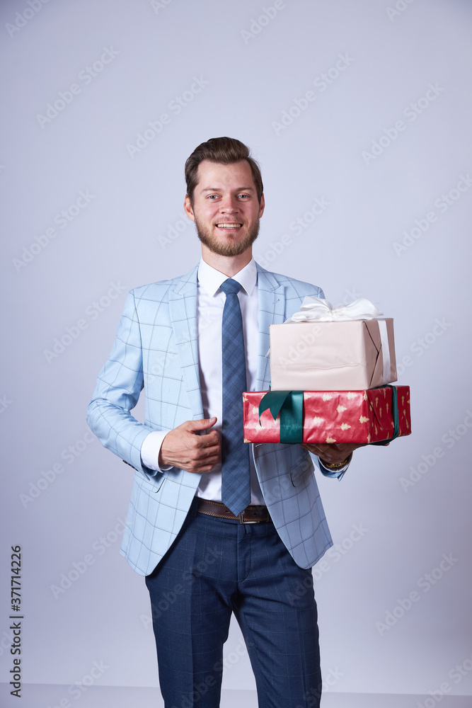 A businessman in a blue suit stands on a white background and holds two christmas gifts in his hands, looking into the camera. A businessman in a blue suit stands on a white background and holds two christmas gifts in his hands, looking into the camera.