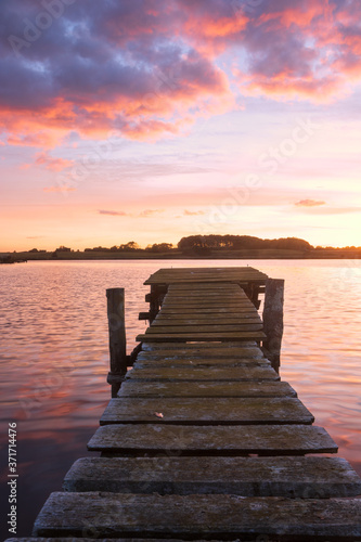 Fototapeta Naklejka Na Ścianę i Meble -  rustikaler Steg mit Moos am See mit angestrahlten Wolken am Abendhimmel, Hochformat