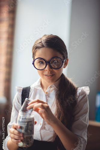 Girl in eyeglasses putting money into a jar