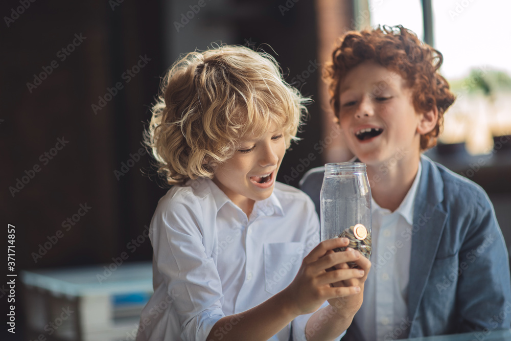 Two boys looking at the jar with coins and looking interested