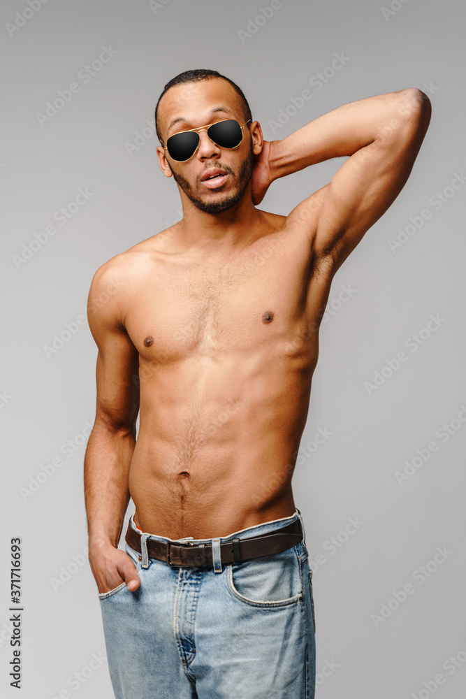 Sexy young muscular african american man shirtless wearing sunglasses over light grey background