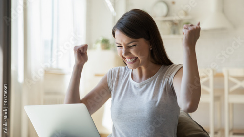 Konstfotografi Excited overjoyed young woman sitting on couch at home with laptop screen feelin