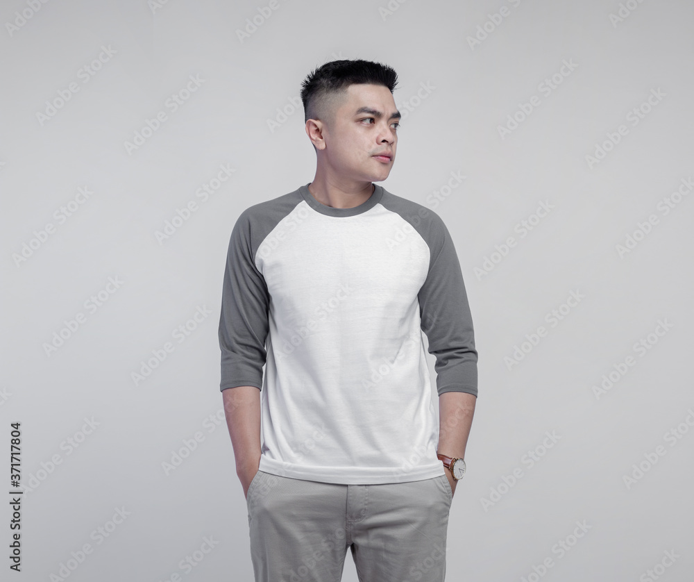 Young handsome man wearing raglan t-shirt with grey and white color isolated on background Young handsome man wearing raglan t-shirt with grey and white color isolated on background