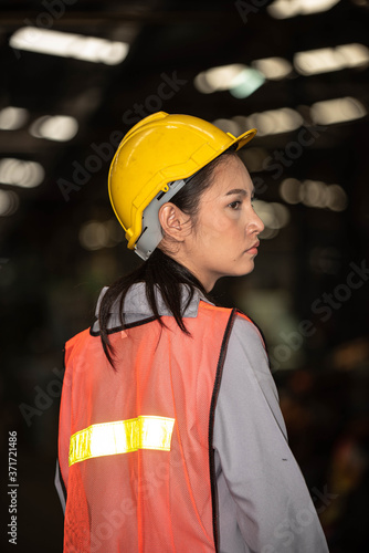 Portrait of young beautiful Asian woman technician or industrial worker with hard hat and vest working machine in Factory of manufacturing place and Bokeh on Background