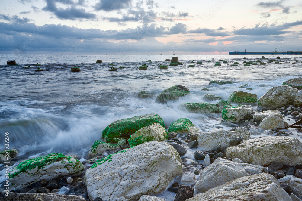 Long exposure of the coastal landscape of Imereti Adler beach with warm evening light, when the waves wash over rocks covered with seaweed