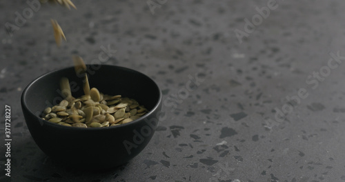 dried pumpkin seeds falling into black bowl on terrazzo countertop
