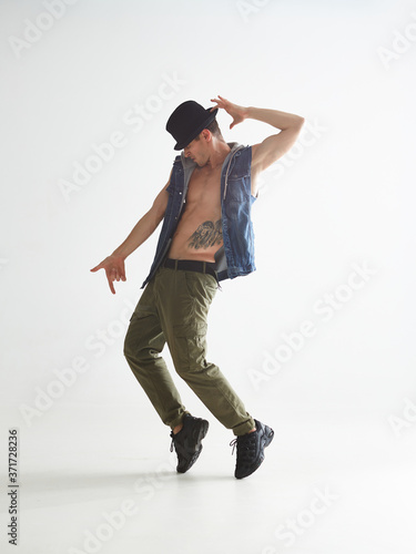 Fototapeta Stylish young guy breakdancer in hat dancing moonwalk in studio isolated on white background