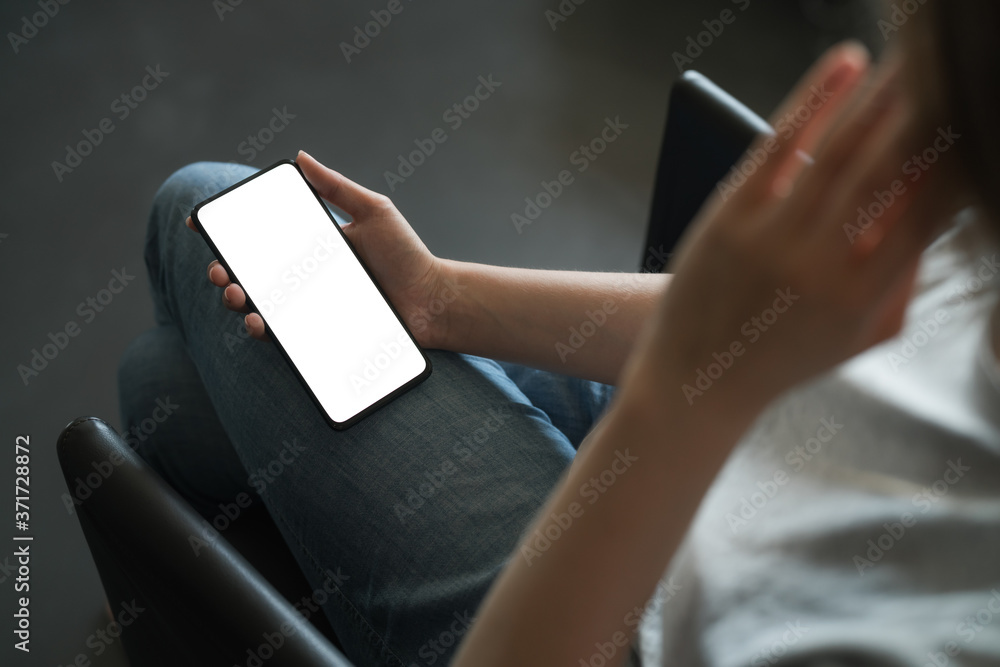 Young woman sitting in chair and holding smartphone with white screen Young woman sitting in chair and holding smartphone with white screen