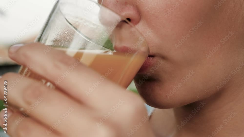 Woman is drinking peach juice. Side view of female hand bring glass with peach juice to their mouth and drink it on sunny day in nature. Close-up Woman is drinking peach juice. Side view of female hand bring glass with peach juice to their mouth and drink it on sunny day in nature. Close-up